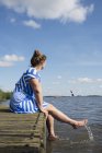 Woman sitting on jetty in the Frisian lake district in vintage dress, Sneek, Friesland, Países Baixos — Fotografia de Stock