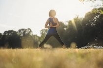 Donna matura nel parco, in piedi in posizione yoga, mani dietro la schiena, vista posteriore — Foto stock