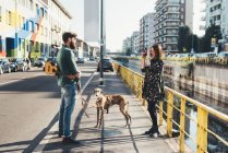 Young woman photographing boyfriend and dog by canal using instant camera — Stock Photo