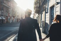 Вид сзади на крутую пару, прогуливающуюся по освещенной солнцем улице — стоковое фото