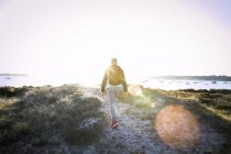 Вид сзади на молодого человека, идущего вдоль песчаных дюн — стоковое фото