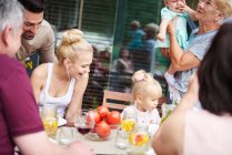 Familia de tres generaciones con bebé y niña en el almuerzo familiar en la mesa del patio - foto de stock