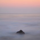 Uma rocha no mar nebuloso ao nascer do sol — Fotografia de Stock