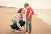 Молода жінка підкидає синові джинси на пляжі — стокове фото