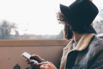 Junger Mann sitzt in U-Bahn, hält Smartphone in der Hand und schaut aus dem Fenster — Stockfoto
