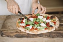 Cropped image of Woman cutting homemade pizza on chopping board — Stock Photo