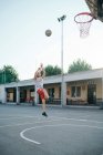Hombre saltando al aro de baloncesto en el patio de recreo - foto de stock