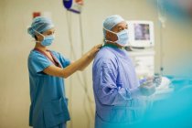 Enfermera atar máscara en cirujano - foto de stock