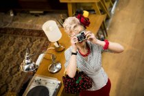 Quirky woman taking photographs on vintage camera in antiques emporium — Stock Photo