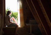 Девочка-подросток сидит на подоконнике спальни и смотрит на солнечный свет. — стоковое фото