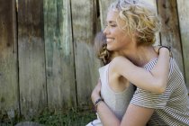 Mutter und Tochter umarmen sich, Holzzaun im Hintergrund — Stockfoto