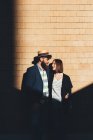 Cool couple gazing at each other by sunlit brick wall — Stock Photo