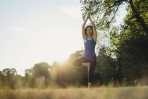 Зрелая женщина в парке, балансирует на одной ноге, в положении йоги, вид с низкого угла — стоковое фото