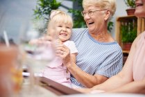 Старшая женщина смеется с внучкой малыша за семейным обедом на патио — стоковое фото