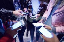 Sección media de amigos adultos jóvenes de pie en círculo mirando los teléfonos inteligentes - foto de stock