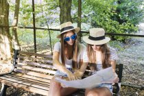 Двоє молодих друзів сидять на лавці, дивлячись на карту в парку — стокове фото