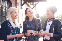 Three young female friends chatting on sunlit city street — Stock Photo