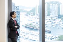 Geschäftsmann blickt aus Bürofenster auf Hafen — Stockfoto