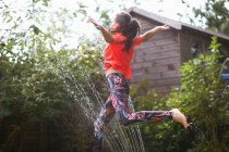 Дівчина стрибає над садовим спринклером — стокове фото