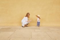 Donna incinta e figlia che giocano vicino al muro giallo — Foto stock