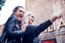 Две молодые женщины делают селфи на смартфоне на городской улице — стоковое фото