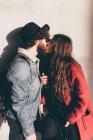 Young couple standing against wall, kissing — Stock Photo