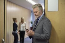Reifer Geschäftsmann mit Smartphone im Büro — Stockfoto