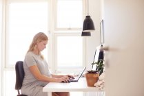 Side view of pregnant young woman typing on laptop at desk — Stock Photo