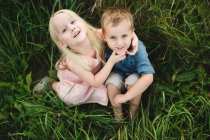 Мальчик и девочка сидят в высокой траве вместе, смотрят в камеру — стоковое фото