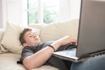Хлопчик-підліток лежить на дивані дивиться на ноутбук — стокове фото