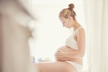 Вид сбоку на беременную женщину, обнимающую живот — стоковое фото
