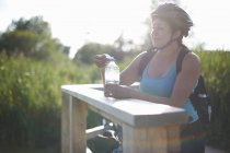 Жінка-велосипедистка робить перерву і тримає пляшку води — стокове фото