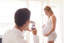 Homme photographiant petite amie enceinte sur smartphone — Photo de stock