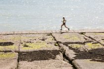 Jovem mulher correndo ao longo da parede do mar — Fotografia de Stock