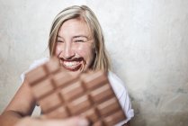 Portrait of woman eating bar of chocolate, chocolate around mouth — Stock Photo
