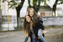 Portrait of young woman giving best friend a piggy back in park — Stock Photo