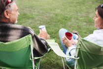 Couple mature assis dans des chaises de camping, tenant des tasses en étain, vue arrière — Photo de stock