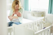 Mother sitting on bed, holding newborn baby — Stock Photo
