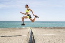 Side view of woman runner jumping over gap in bridge — Stock Photo