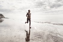 Молодая бегунья бегает босиком вдоль берега на пляже — стоковое фото
