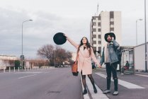 Молодая пара на улице, держась за руки, молодая женщина, держа шляпу в руке, вызывая такси — стоковое фото