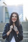 Портрет молодой женщины, держащей воротники куртки, улыбающейся, татуировки на руках — стоковое фото