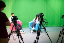 Молодые студенты и студентки колледжа практикуют в телевизионной студии с зеленым экраном — стоковое фото