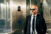 Reifer Geschäftsmann mit Sonnenbrille steht im Fahrstuhl — Stockfoto