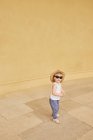 Toddler girl standing by yellow wall — Stock Photo