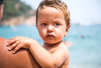 Über-die-Schulter-Ansicht einer Mutter, die ihren kleinen Sohn am Strand trägt, Begur, Katalonien, Spanien — Stockfoto