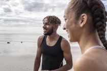 Corredores jóvenes masculinos y femeninos sonriendo en la playa - foto de stock