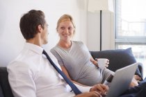 Pregnant couple looking to each other on sofa — Stock Photo