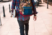 Vista posteriore ritagliata dello skateboarder maschile che cammina lungo il marciapiede — Foto stock