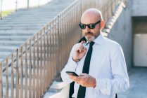 Reifer Geschäftsmann trägt Jacke über der Schulter und nutzt Smartphone — Stockfoto
